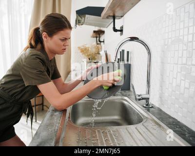 Femme fatiguée et irritée mains sans gants lave la vaisselle avec une éponge de lavage de vaisselle, des tâches ménagères, pas de lave-vaisselle, consommation d'eau élevée. Élégant Banque D'Images