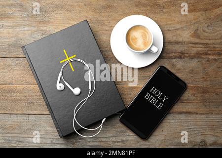 Bible, téléphone, tasse de café et écouteurs sur fond de bois, plat. Livre audio religieux Banque D'Images