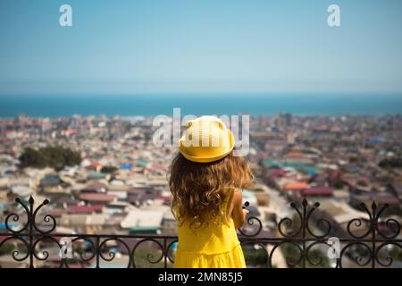 Une fille touristique dans un chapeau jaune et une sundress regarde d'une hauteur sur la terrasse d'observation de la ville. Visite touristique. L'enfant s'est perdu, recherchant f Banque D'Images