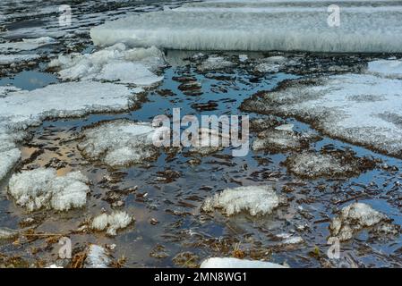 Les restes de la dernière glace de printemps sur la rivière fondent près de la rive dans l'eau avec le reflet du ciel. Banque D'Images