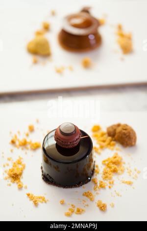Gros plan d'un petit gâteau à la mousse au chocolat noir avec garniture au macaron français, biscuit et chapelure d'amande sur l'assiette. Fond moderne en dessert. Banque D'Images