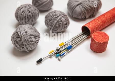 Coudre l'arrière-plan. Jeu d'aiguilles à tricoter en boîte rouge, bouquet de fils gris. Boules de laine sur fond blanc, ensemble de tricot de style rétro. Passe-temps, hiver Banque D'Images