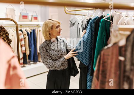 Élégante jeune femme choisissant des vêtements dans la boutique de luxe au centre commercial Banque D'Images