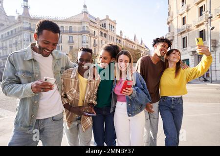 Groupe d'amis multiethniques accrochant à l'extérieur dans la rue, marchant et riant, utilisant le téléphone. Banque D'Images
