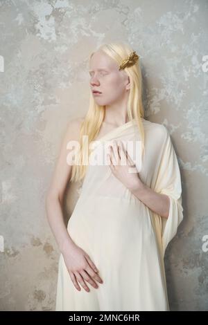 Jeune femme albino sereine en tenue blanche gardant les yeux fermés tout en se tenant près du mur en marbre devant l'appareil photo pendant la séance photo Banque D'Images