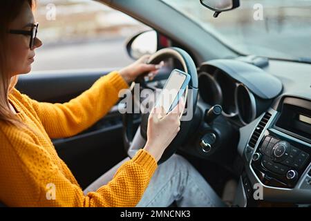 Jeune femme conducteur utilisant un téléphone portable en conduisant la voiture, conduite non sécuritaire Banque D'Images