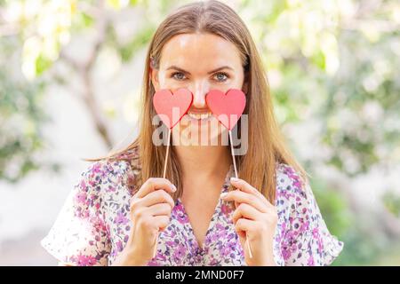 Femme avec deux coeurs décoratifs dans ses mains souriant sur fond naturel Banque D'Images