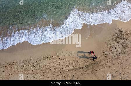 Paysage aérien de drone de personnes non reconnues marchant dans une plage de sable en hiver. Des vagues venteuses s'écrasant sur le rivage Banque D'Images