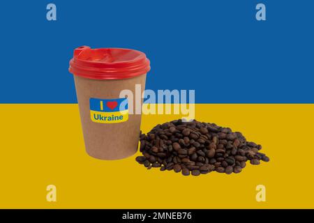 Tasse de café en papier avec un autocollant patriotique « I love Ukraine » et une poignée de grains de café sur le fond du drapeau de l'Ukraine (gros plan) Banque D'Images