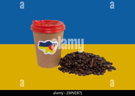 Tasse de café en papier avec un autocollant patriotique « I love Ukraine » et une poignée de grains de café sur le fond du drapeau de l'Ukraine (gros plan) Banque D'Images