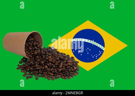 Une tasse en papier jetable retournée remplie de grains de café torréfiés sur le fond du drapeau du Brésil (gros plan) Banque D'Images