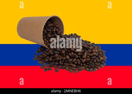 Une tasse en papier jetable retournée remplie de grains de café torréfiés sur le fond du drapeau colombien (gros plan) Banque D'Images