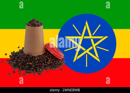 Une tasse en papier jetable retournée avec un couvercle rempli de grains de café torréfiés sur le fond du drapeau éthiopien (gros plan) Banque D'Images