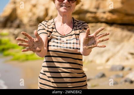 Femme âgée méconnue montrant ses mains de paume recouvertes de sable Banque D'Images