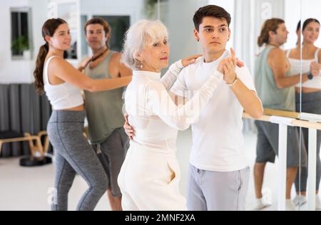 Une jolie femme âgée et un jeune homme répètent une danse en couple dans un studio moderne. Banque D'Images