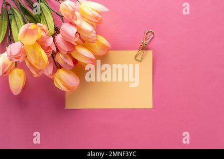 Concept printanier avec tulipes jaunes et roses, un notecard jaune tenu par un trombone doré sur fond rose. Espace vide pour le devis ou le message Banque D'Images