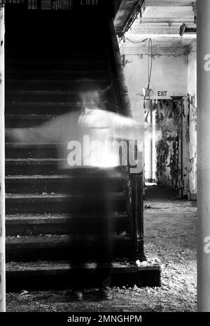 Homme transparent aux armes étirées debout à l'escalier du bâtiment abandonné Banque D'Images