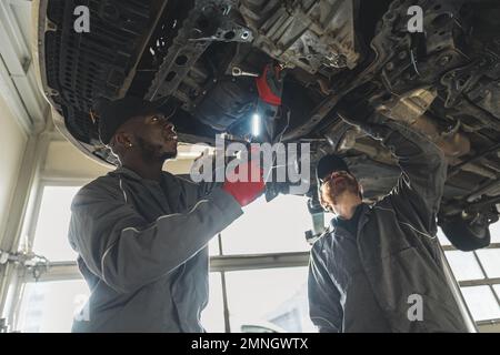 Deux mécaniciens remplaçant l'embrayage d'une voiture soulevée à l'aide d'outils dans un atelier de réparation automobile. Photo de haute qualité Banque D'Images