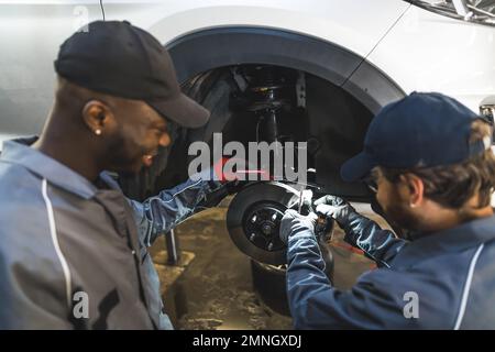 Mécanicien remplaçant les roues d'une voiture de luxe blanche à l'aide d'outils dans un atelier de réparation automobile. Photo de haute qualité Banque D'Images