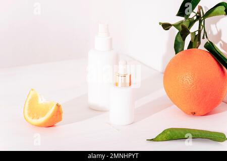 Flacons de sérum à usage cosmétique et fruits orange sur fond blanc. Concept de cosmétiques naturels, maquette Banque D'Images