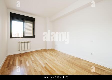 Salle de séjour vide avec murs blancs, sol stratifié nouvellement installé, fenêtre en aluminium noir avec store et radiateur en dessous Banque D'Images