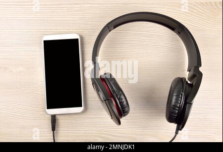 Casque noir sur table en bois avec smartphone Banque D'Images