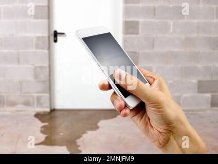 Une main tenant un smartphone avec des dommages d'eau dans le sous-sol causés par le refoulement d'égout en raison de fond de drain sanitaire obstrué Banque D'Images