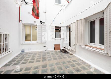 Cour lumineuse d'un bâtiment avec plancher en verre, plantes en pot décoratives, fenêtres avec volets en métal blanc en fer et vêtements suspendus sur des cordes Banque D'Images