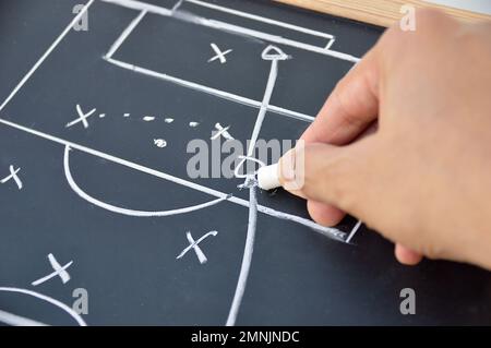 main d'un entraîneur de football dessinant une tactique de jeu de football avec la craie blanche sur le tableau de noir sur fond blanc Banque D'Images