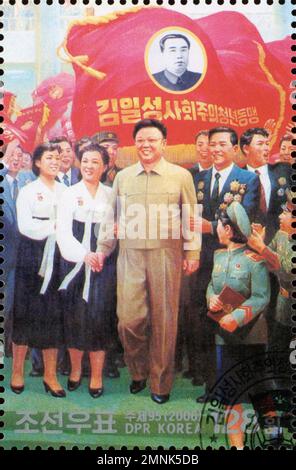 Timbre-poste nord-coréen de 2006 représentant Kim Jong-il et un portrait de Kim il-sung sur un drapeau rouge avec des citoyens. Banque D'Images