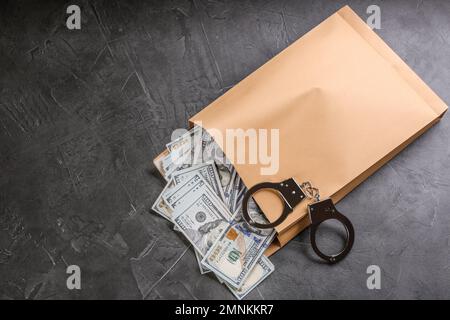 Enveloppe avec billets de dollars et menottes sur table en pierre grise, vue du dessus. Concept de corruption Banque D'Images