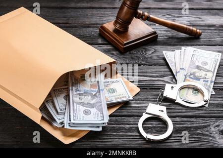Enveloppe avec billets de dollars et menottes sur table en bois noir. Concept de corruption Banque D'Images