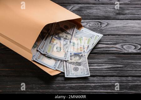 Enveloppe avec billets en dollars sur table en bois noir, gros plan. Concept de corruption Banque D'Images