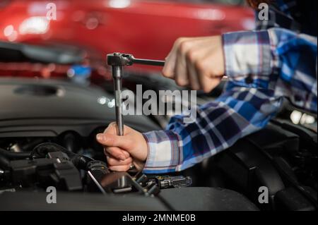 Mécanique automobile femelle en dévissant un écrou pour remplacer une bougie d'allumage de voiture. Banque D'Images