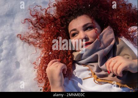 Vue de dessus d'une femme aux cheveux rouges et gras qui s'allonge sur la neige. Banque D'Images