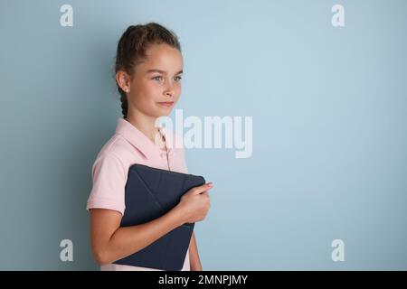 Petite adolescente émotive un arrière-plan bleu isolé avec une tablette dans ses mains. Banque D'Images