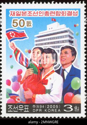 Timbre-poste nord-coréen de 2005 marquant le 50ème anniversaire de Chongryon, représentant une famille heureuse avec des drapeaux et des ballons. Banque D'Images