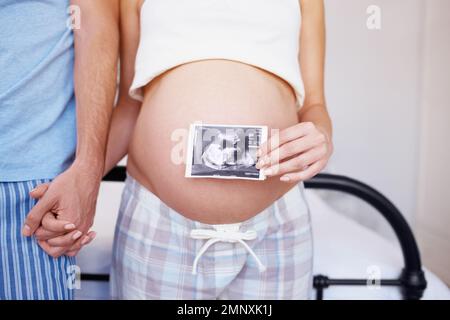 En regardant sur vous... un couple expectant tenant les mains pendant qu'elle place une photo d'échographie sur son ventre. Banque D'Images