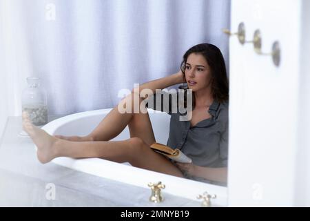 La lecture rêve avec les yeux ouverts. une jeune femme lisant un livre dans une baignoire. Banque D'Images