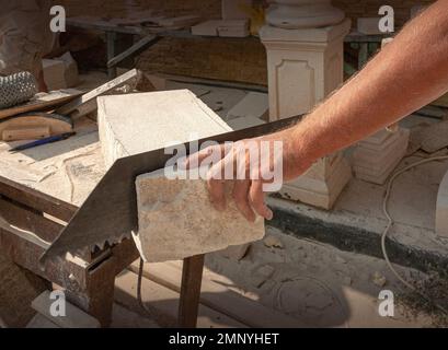 Les mains du sculpteur, qui traite un bloc de pierre blanche sur le bureau avec des outils. Détails de la main Banque D'Images