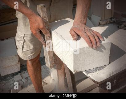 Les mains du sculpteur, qui traite un bloc de pierre blanche sur le bureau avec des outils. Détails de la main Banque D'Images