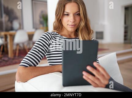 Sa tablette numérique est toujours à portée de main. une jeune femme utilisant une tablette numérique tout en étant assise sur un canapé à la maison. Banque D'Images