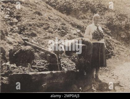 moment vintage / moment amusant vintage / photo vintage / puissance du moment / moments magiques / vieil homme boire d'une source d'eau naturelle à l'extérieur. Il se plie tellement profondément pour atteindre la fontaine naturelle. eau minérale originale du 1920s. sa femme l'attend calmement. Banque D'Images