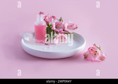 une bouteille ouverte de verre dépoli avec des cosmétiques et une pipette remplie sur une plaque en céramique blanche avec des fleurs printanières délicates. soins pour la peau jeune Banque D'Images