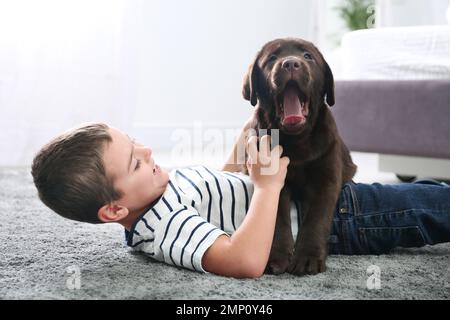 Petit garçon avec un chiot au sol dans la chambre. Chien sympathique Banque D'Images