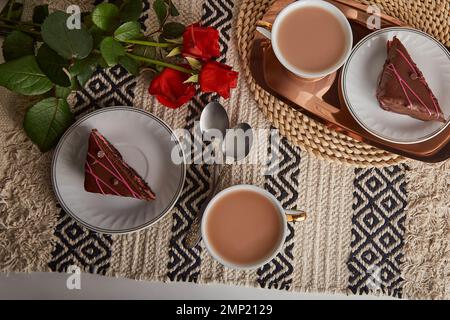 Petit-déjeuner esthétique festif avec gâteaux au chocolat et aux cerises, tasses à café, roses rouges et lattes de Saint-Valentin. Banque D'Images