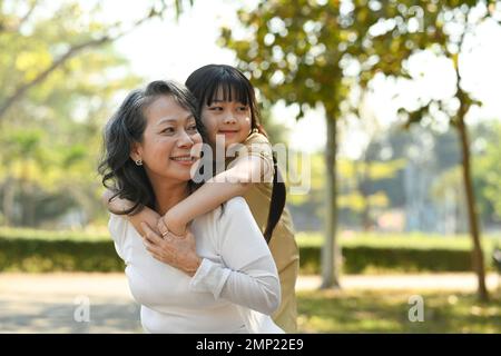 Image d'une grand-mère souriante en âge d'inactivité qui donne une promenade en porcgyback à une petite petite-fille mignonne lors d'une promenade dans le parc Banque D'Images