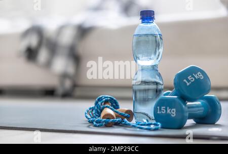 Une corde à sauter, des haltères et une bouteille d'eau sur un tapis à la maison dans le salon. Concept de mode de vie sain. Banque D'Images