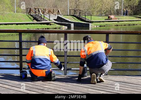 Les travailleurs en uniforme peint la clôture métallique sur un remblai de lac. Travaux de construction et de réparation dans le parc printanier, préparation pour la saison de la plage Banque D'Images