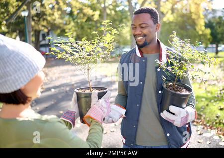 Travail d'équipe, jardinage et homme avec une femme dans un parc heureux et souriant pour la croissance des plantes pour la durabilité dans l'environnement. Bénévole, homme noir et Banque D'Images